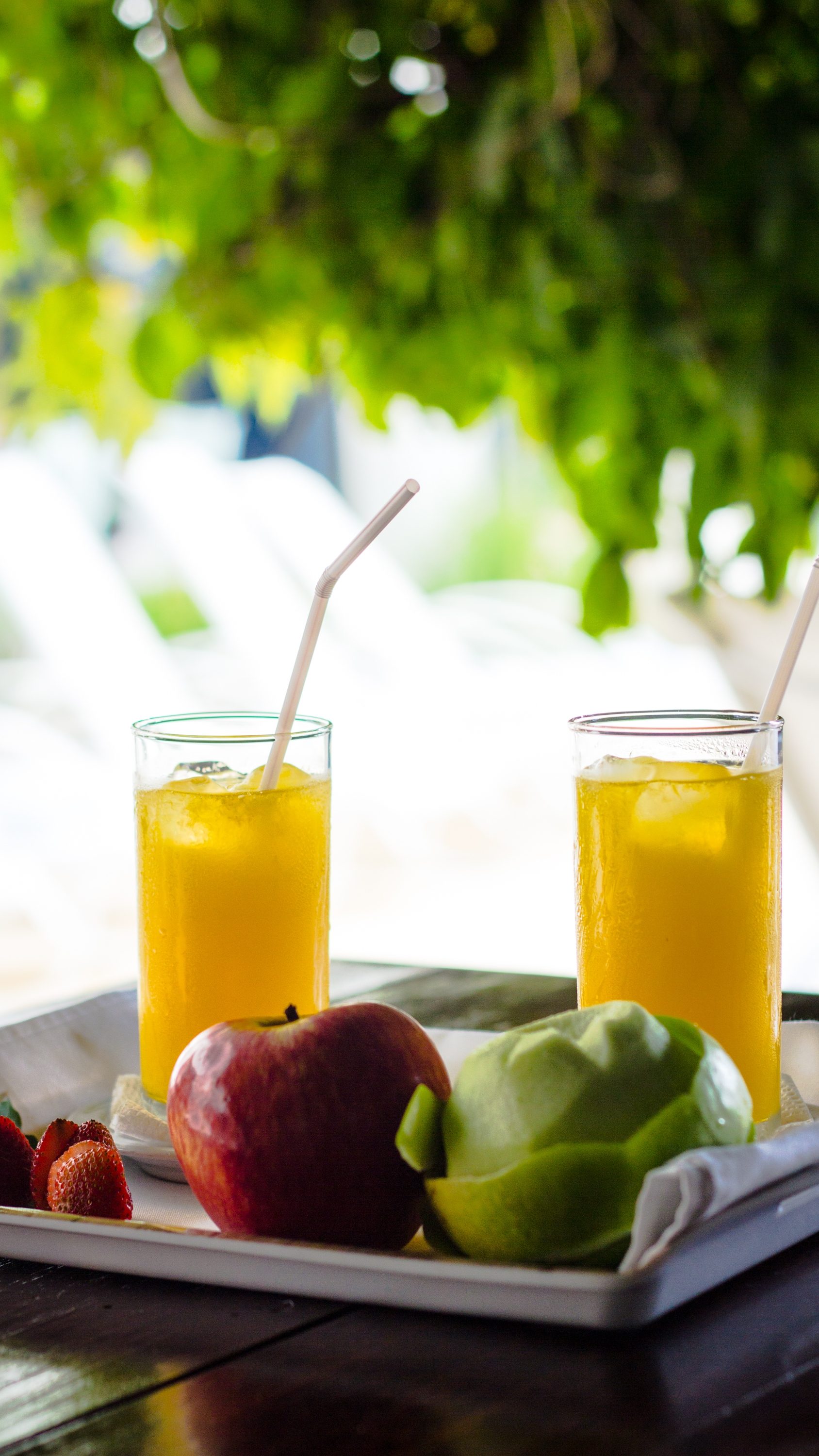 Bandeja de desayuno con jugo de naranja y fruta fresca junto a la piscina