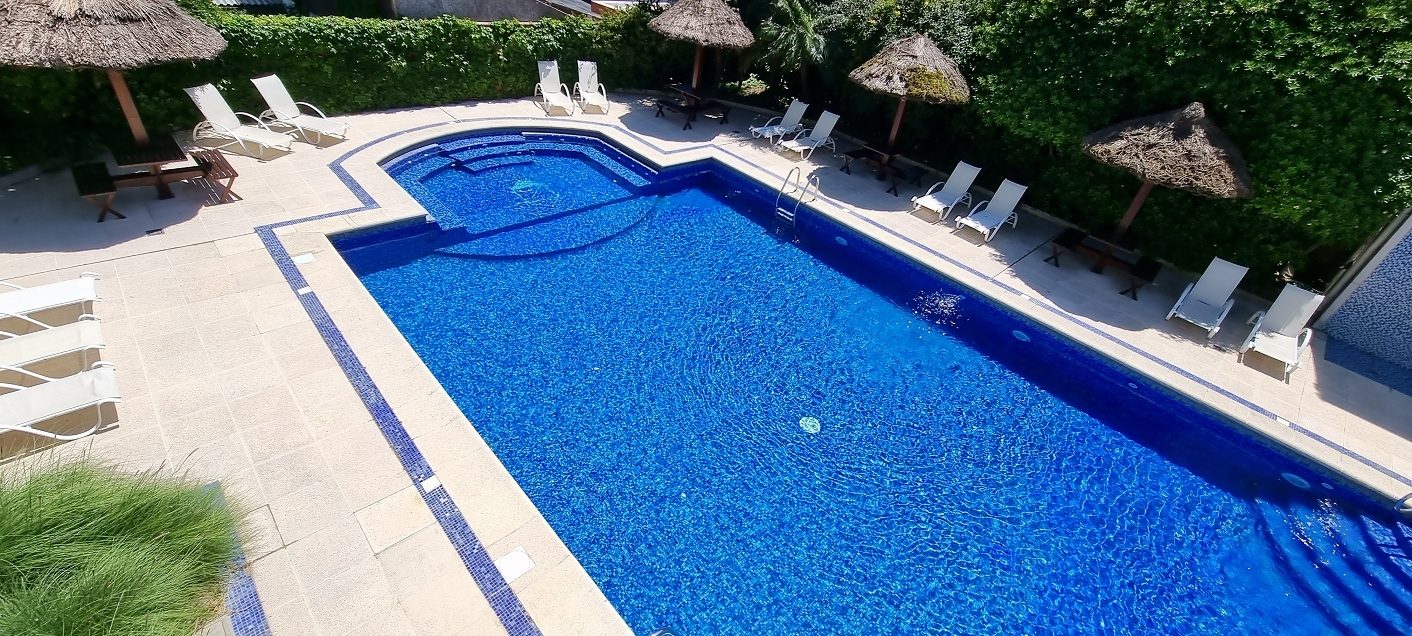 Piscina exterior vista desde arriba, con reposeras y jardín