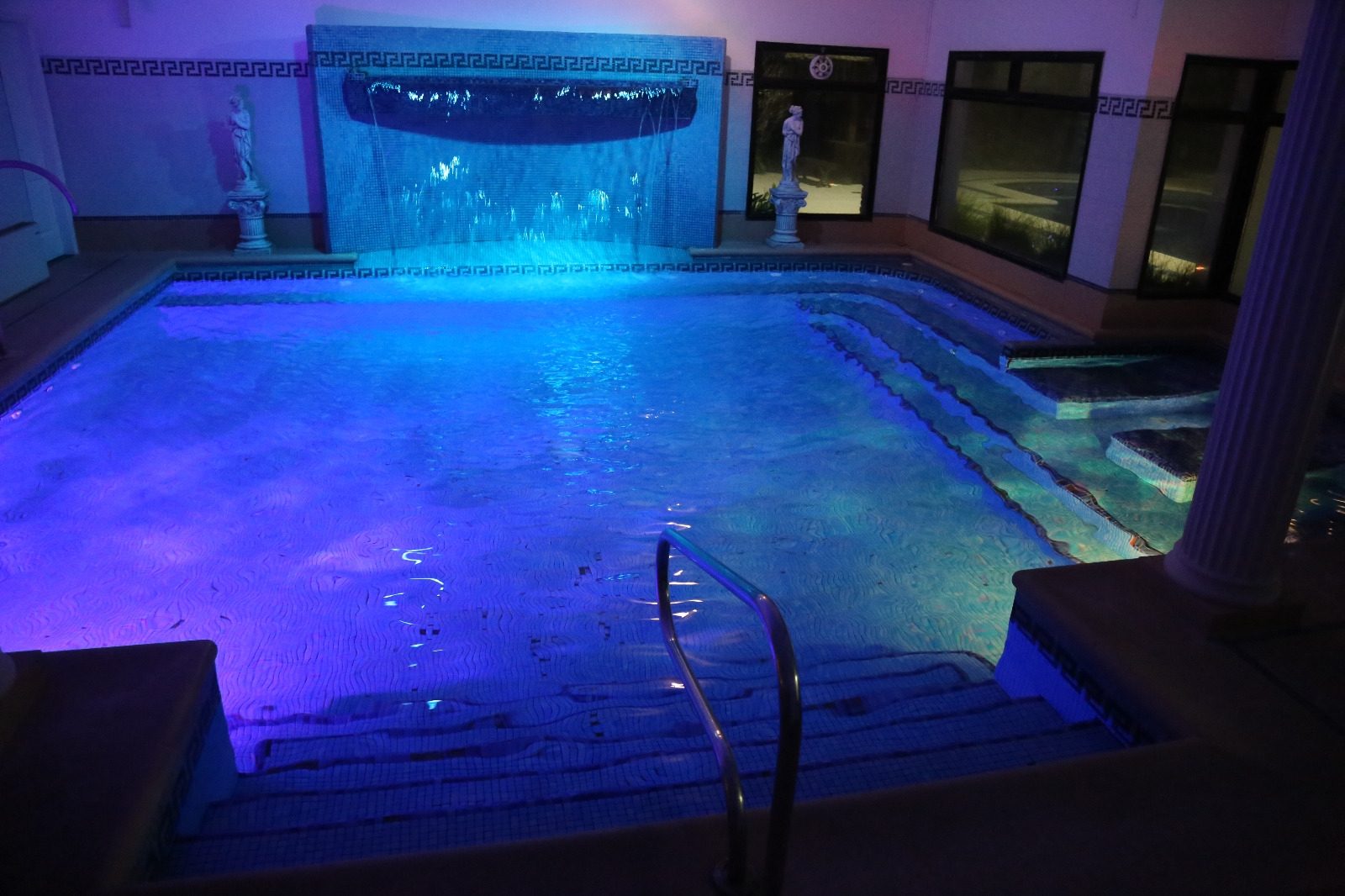 Piscina climatizada cubierta iluminada de azul, con cascada