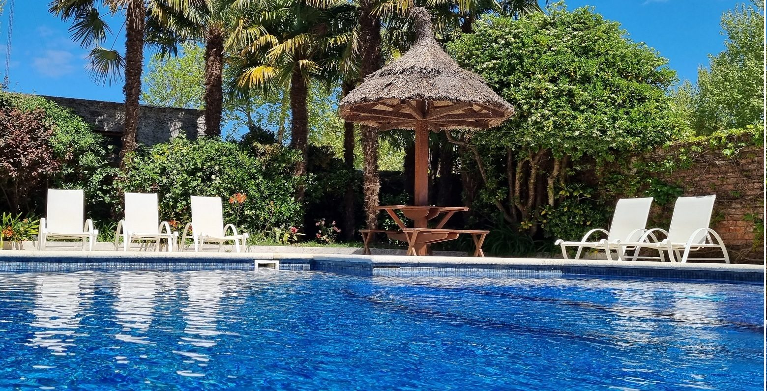 Piscina exterior del Hotel Italiano con reposeras, sombrilla de paja y palmeras